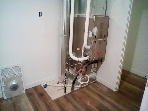 Furnace unit in a corner, ductwork, filter, and flooring. Room with white walls and wooden floor.