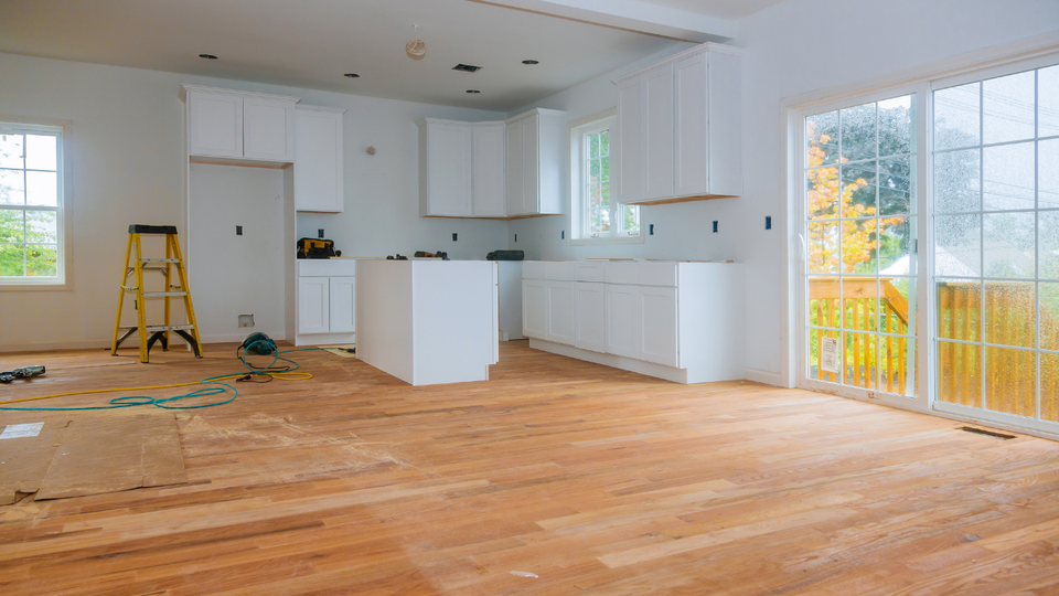 Kitchen renovation in progress, white cabinets, island, wood floor, ladder, tools, and a sliding glass door.