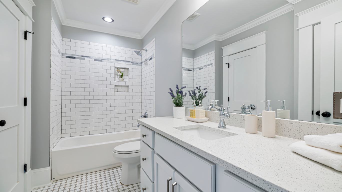 White bathroom with tub, toilet, vanity with sink, and mirror. White and gray tile, and neutral decor.