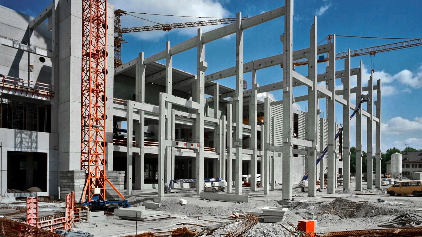 Construction site: concrete framework of a building, cranes, rubble, cloudy sky.