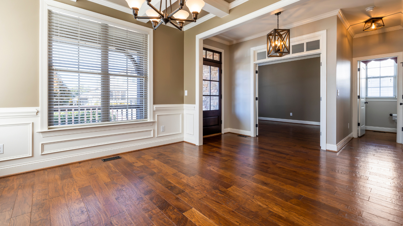 Empty dining room with hardwood floors, large window, and dark wood door.