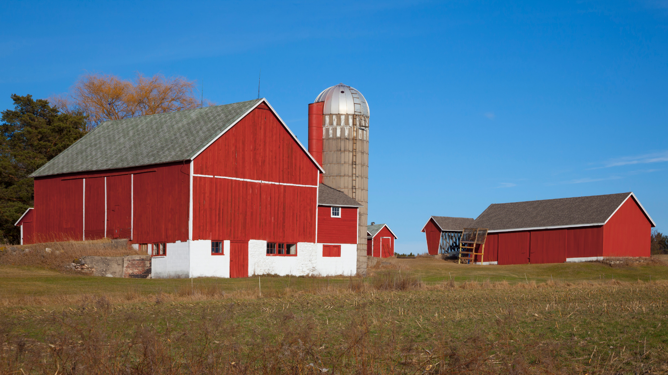 Red barn and silo on a sunny day in a rural field with a clear blue sky.