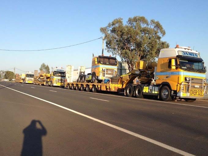 A row of yellow trucks are parked on the side of the road
