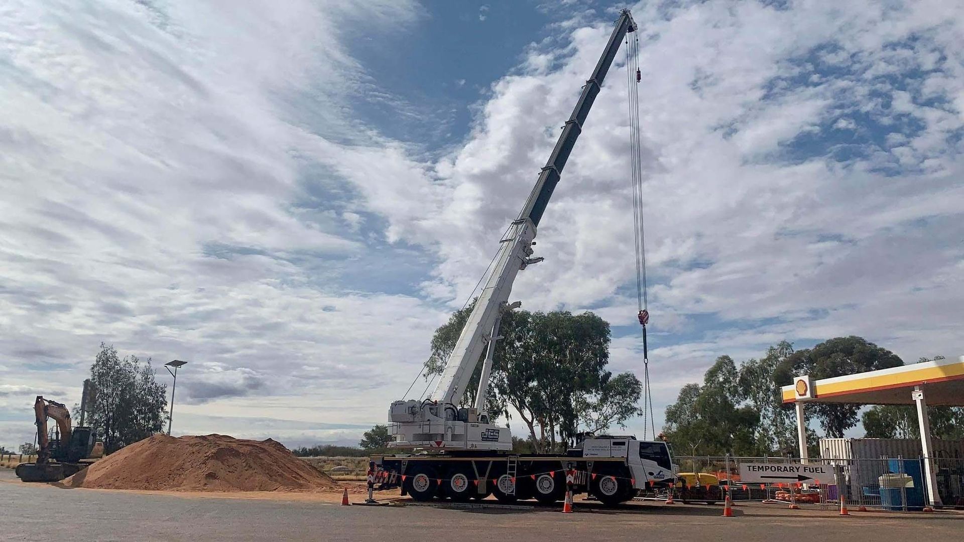 A large crane is sitting on top of a truck in front of a gas station.