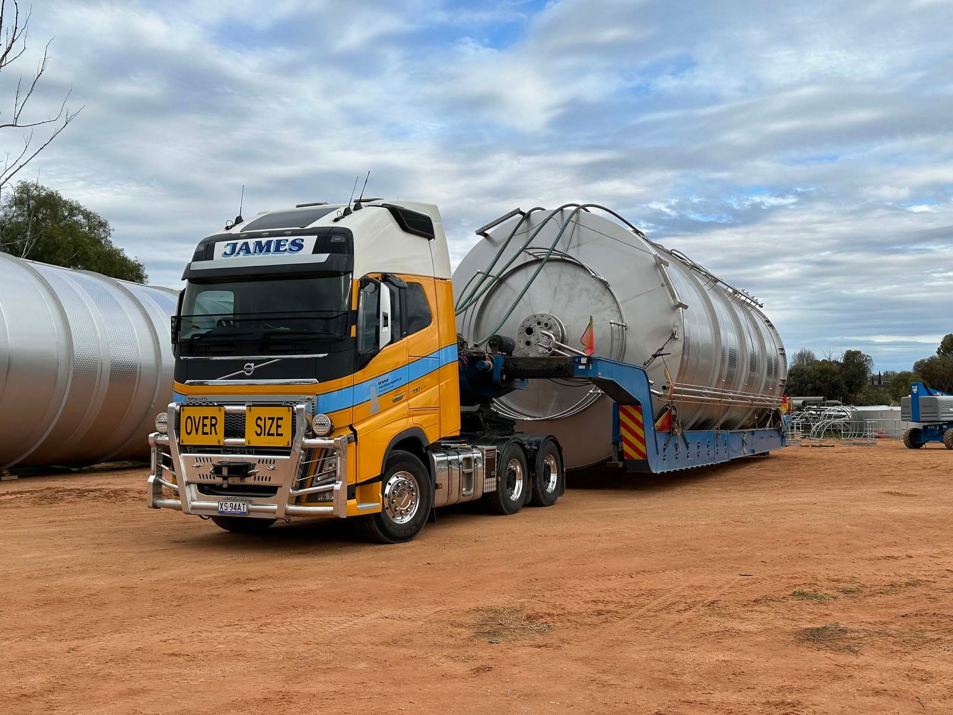 A yellow and white semi truck is carrying a large tank on a trailer.