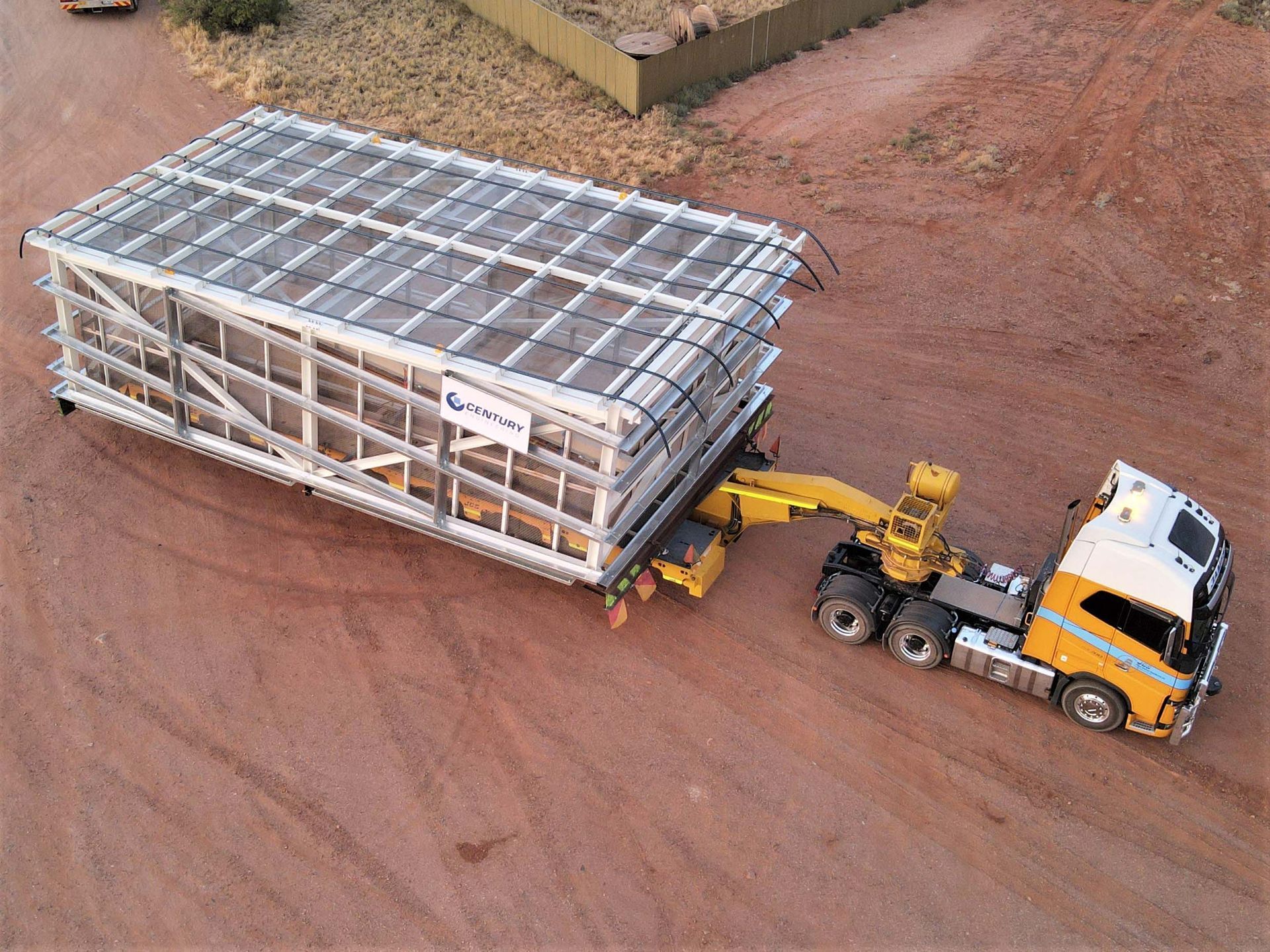An aerial view of a truck pulling a large container on a dirt road.