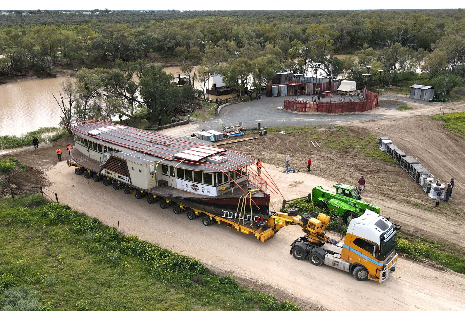 An aerial view of a truck carrying a large boat down a dirt road.