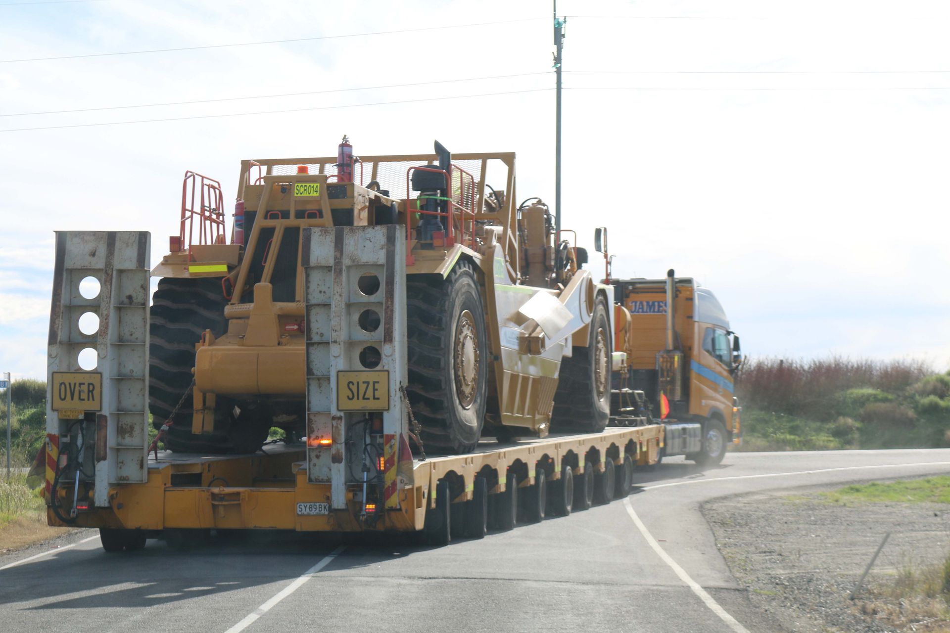 A large yellow truck is driving down a road with a tractor on the back of it