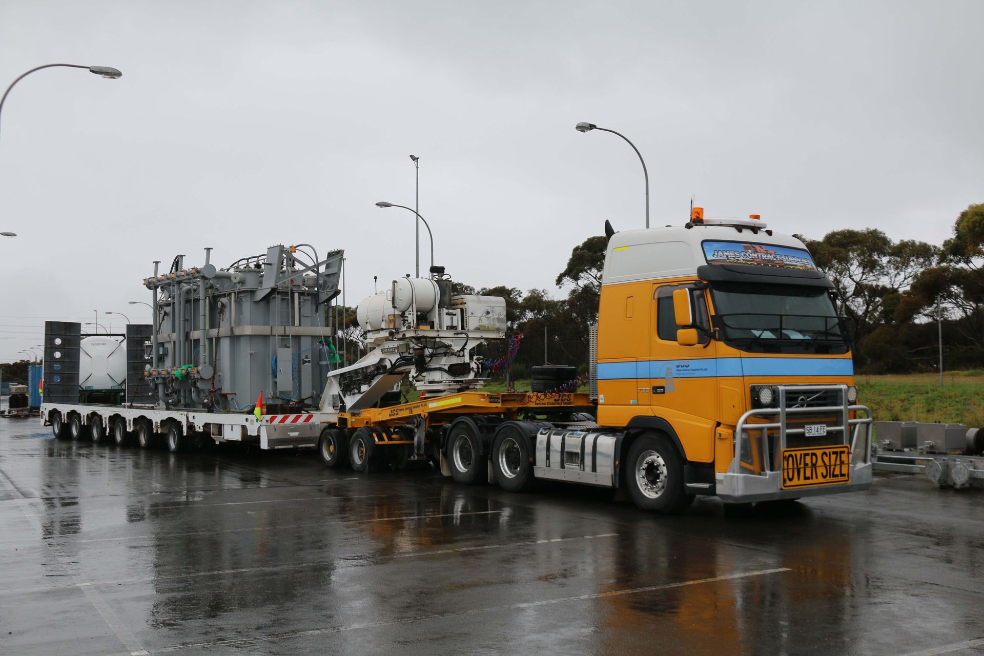 A large yellow truck is driving down a wet road.