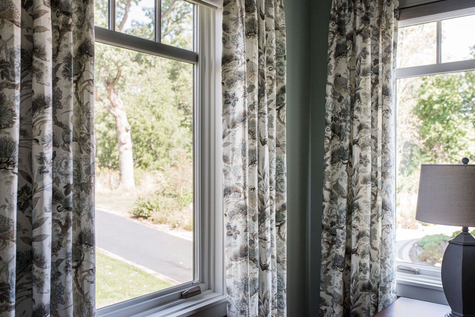 A bedroom with a lamp and a window with curtains on it.