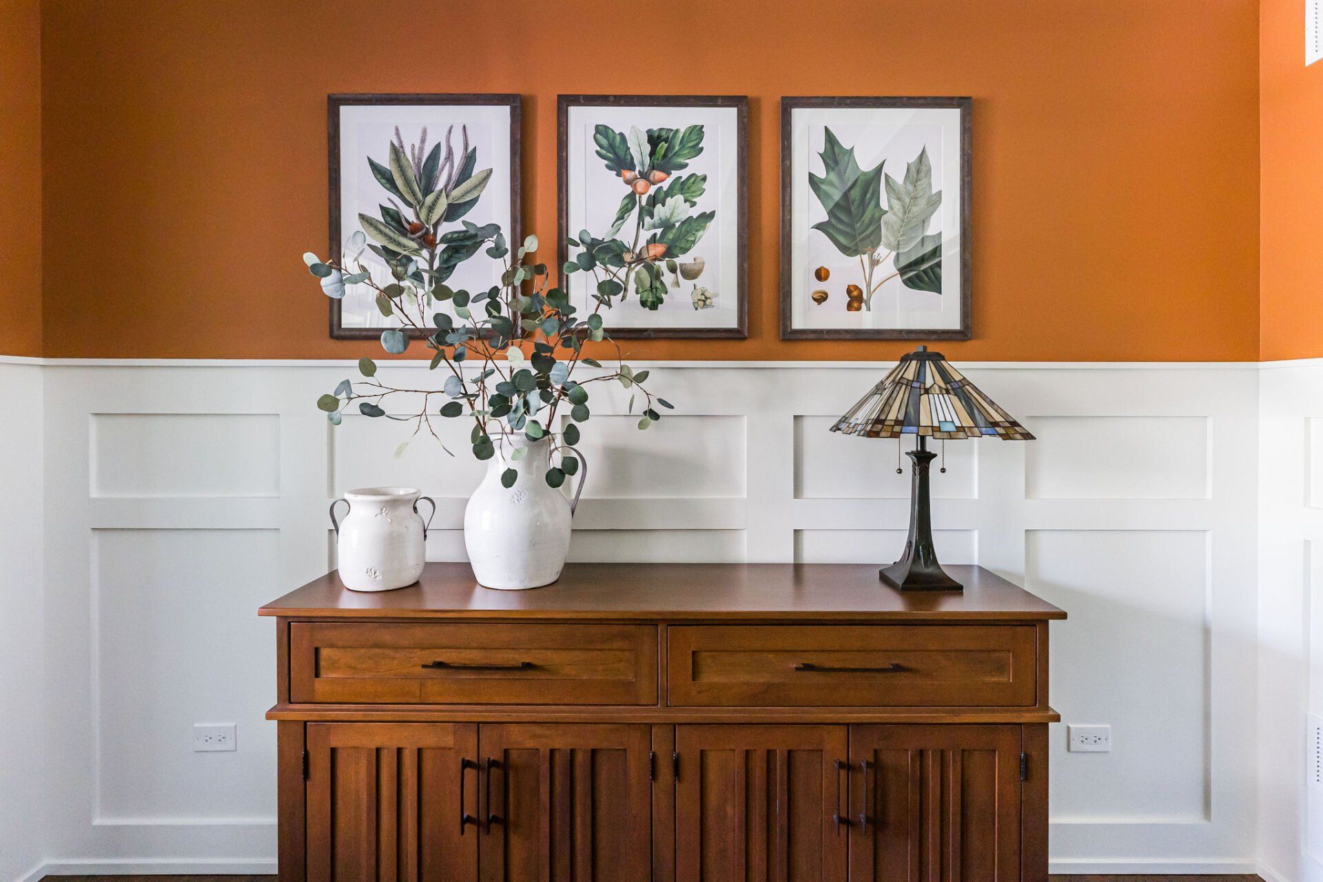 A wooden dresser with a lamp on top of it in a room with orange walls.