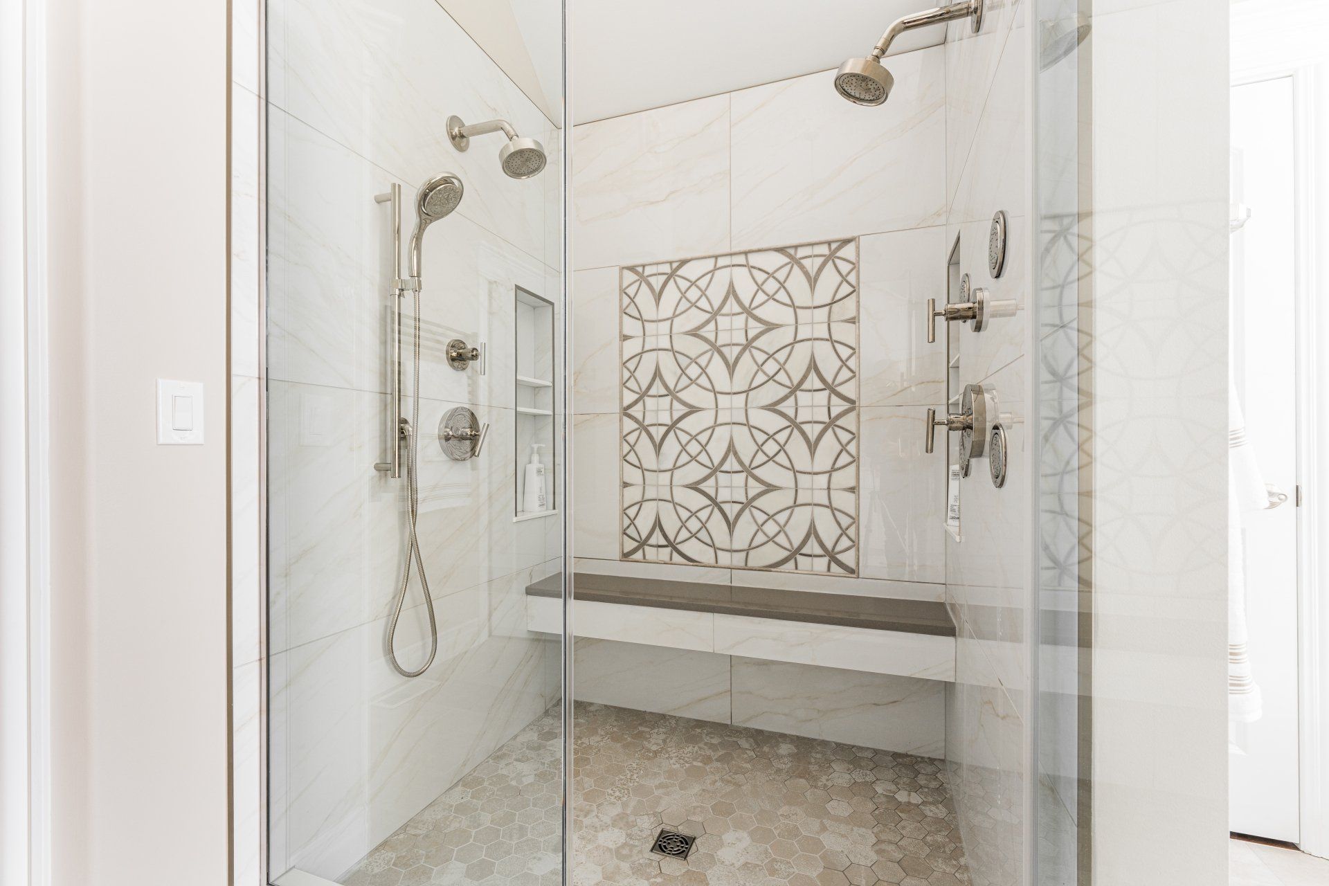 A walk in shower with two shower heads and a bench.