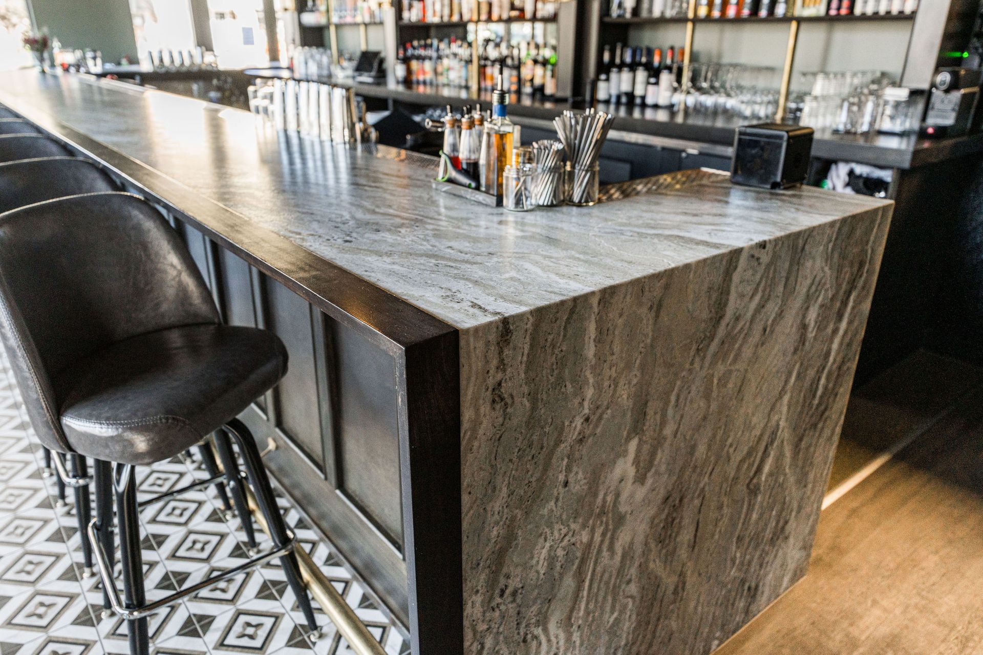 A long bar with a marble counter top and stools in a restaurant.