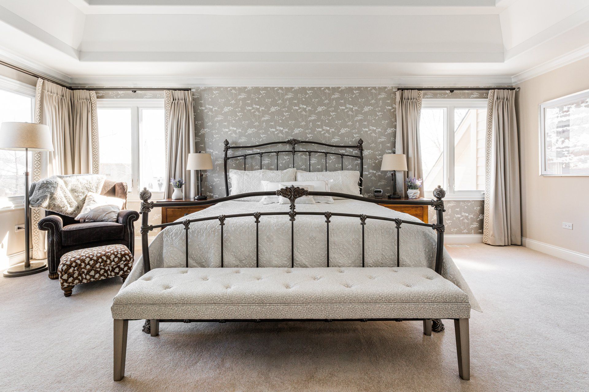 A bedroom with a bed , bench , chair and lamps.