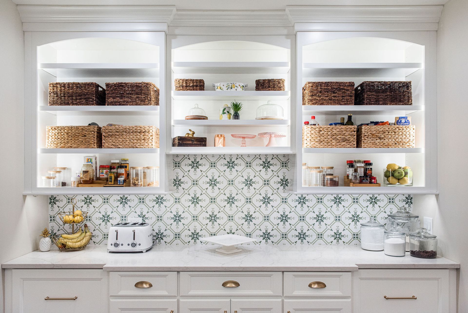 A kitchen with white cabinets , a toaster oven , and wicker baskets on the shelves.