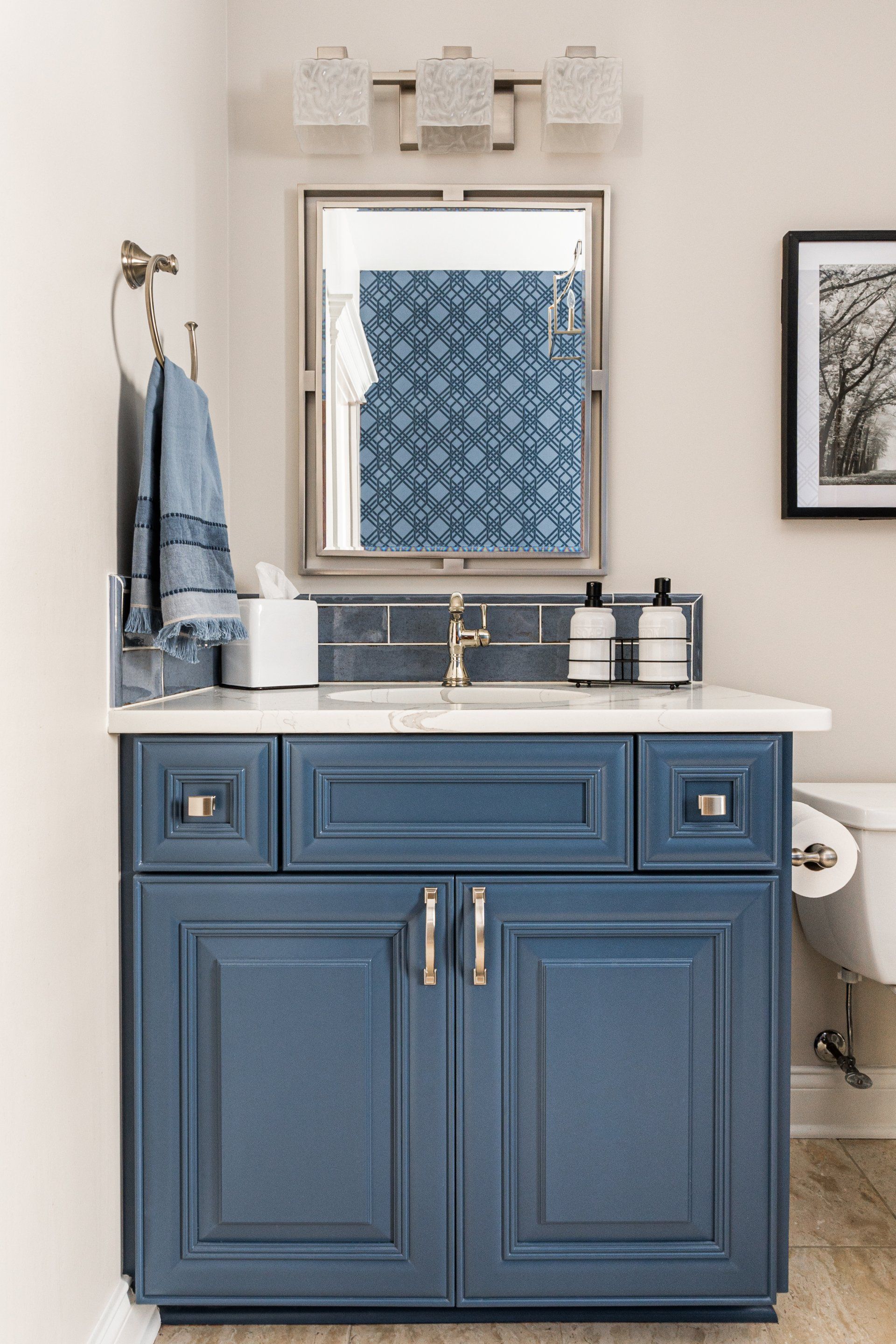 A bathroom with blue cabinets , a sink , a mirror and a toilet.