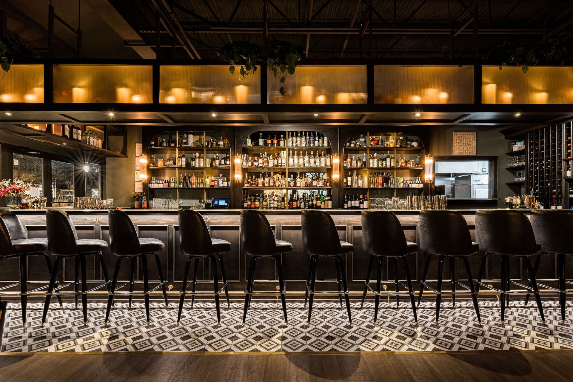 A row of bar stools are lined up in front of a long bar in a restaurant.