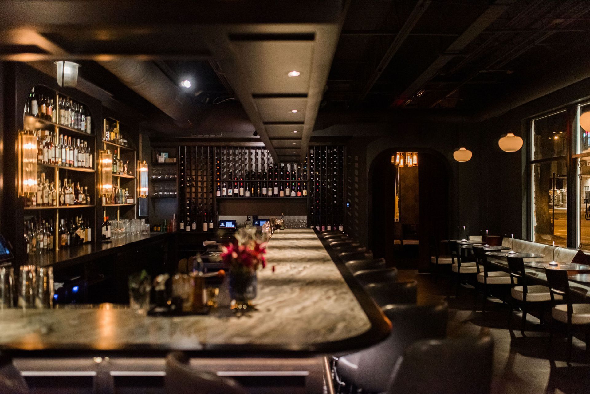 A long bar in a restaurant with tables and chairs.