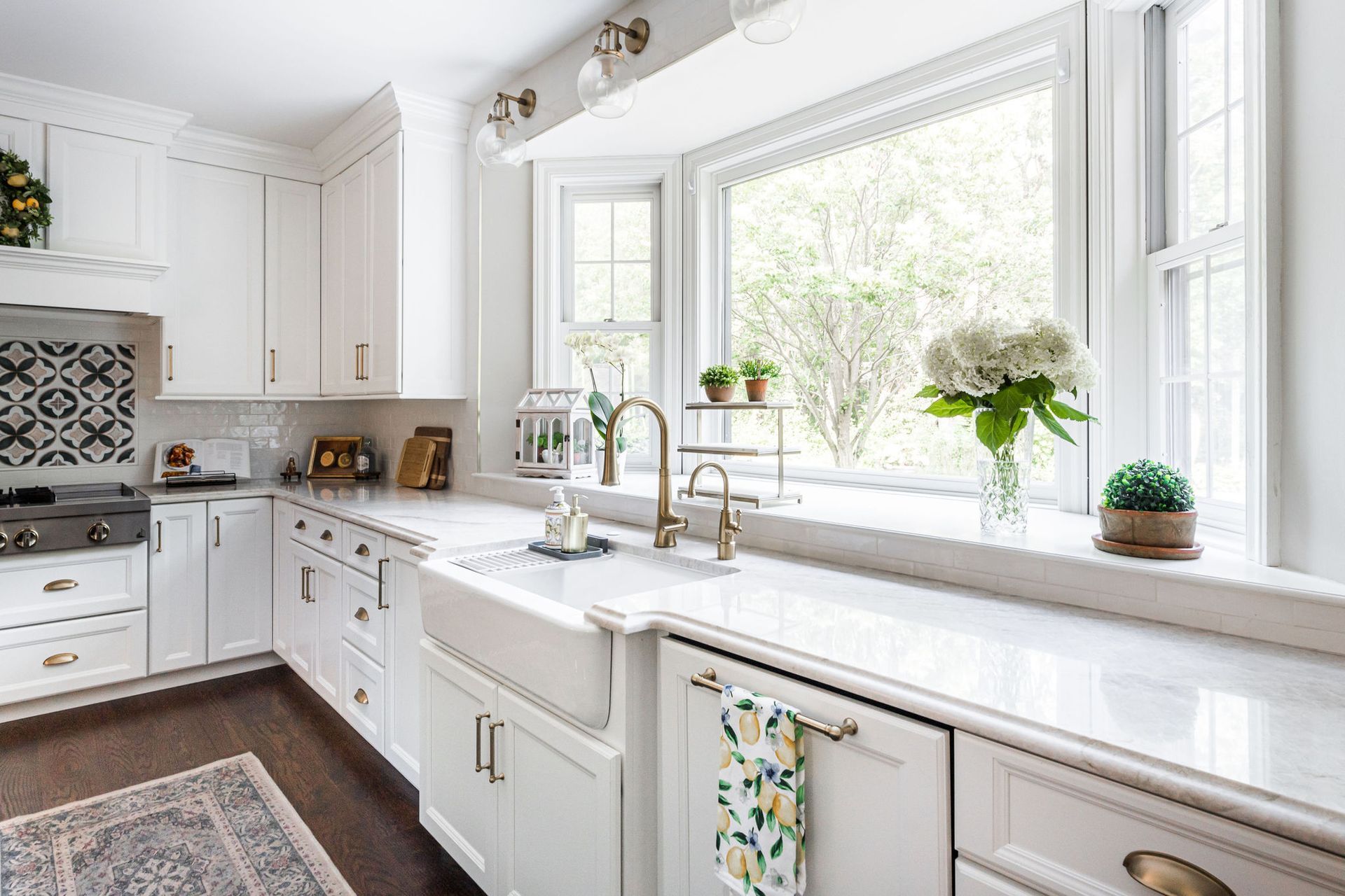 A kitchen with white cabinets , a sink , and a large window.