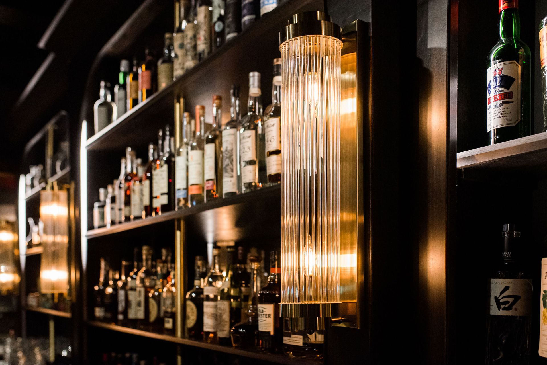 A bar filled with lots of bottles of alcohol and a lamp.