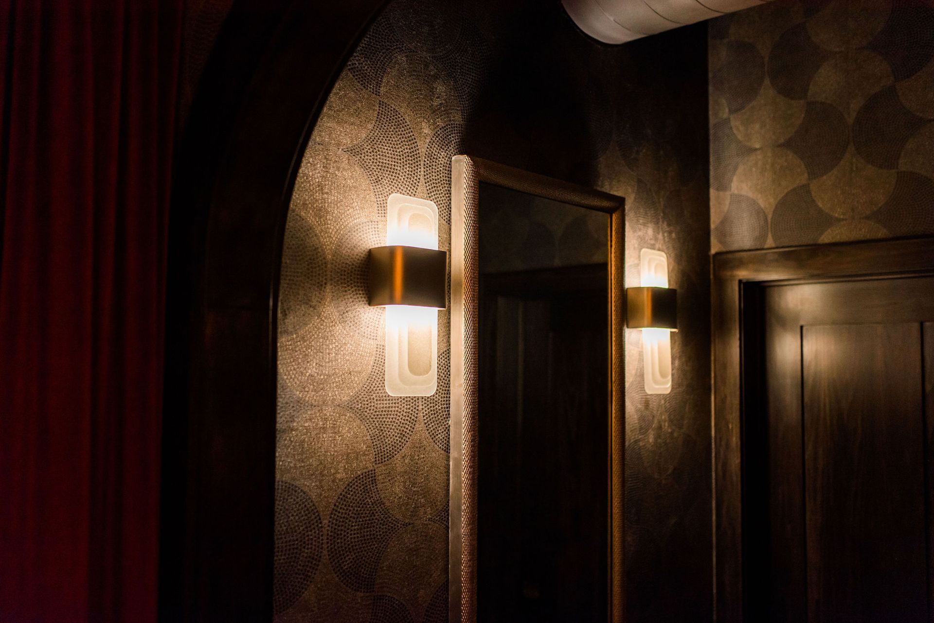 A hallway with a mirror and two lights on the wall.