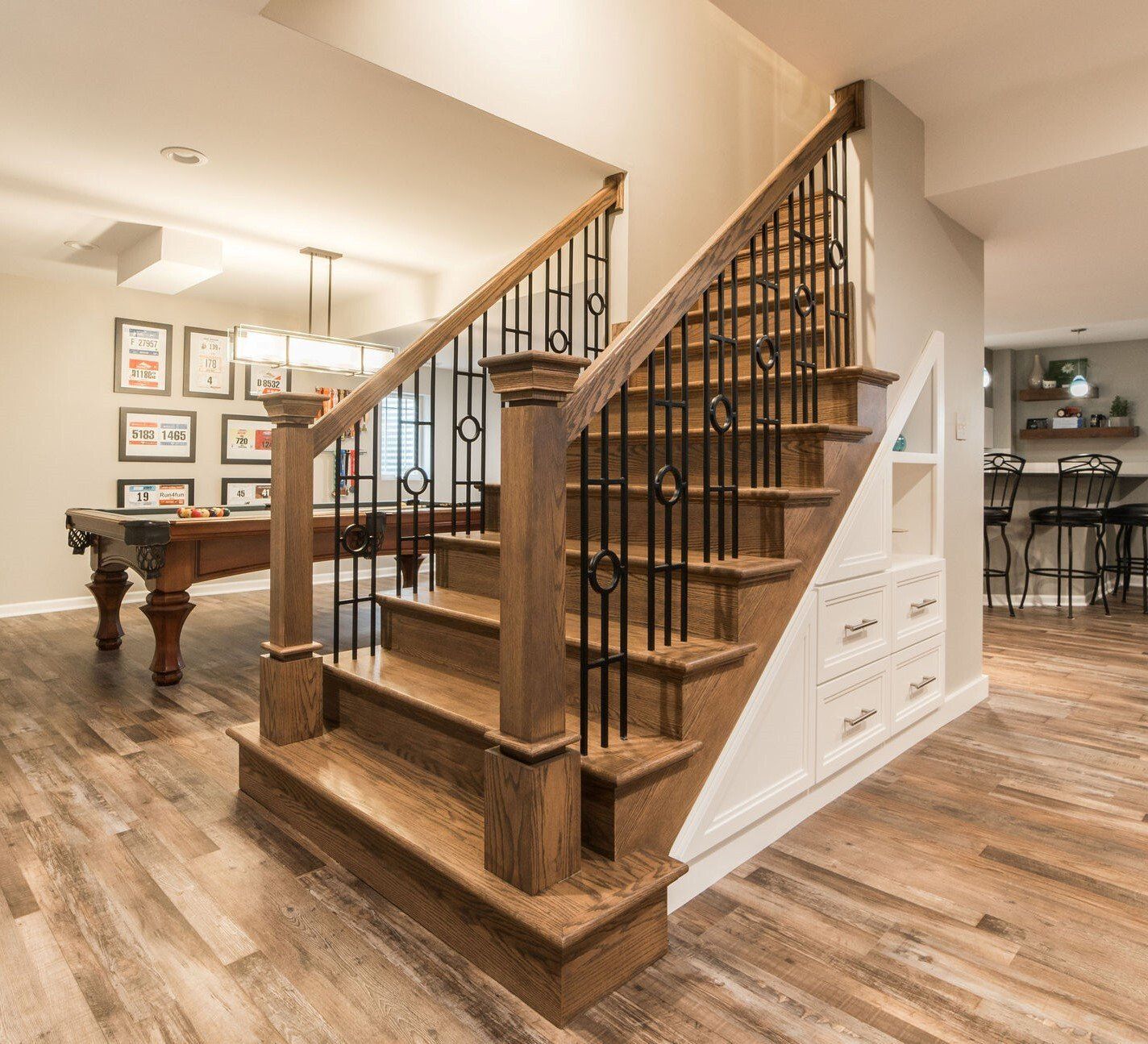 A wooden staircase with a pool table in the background