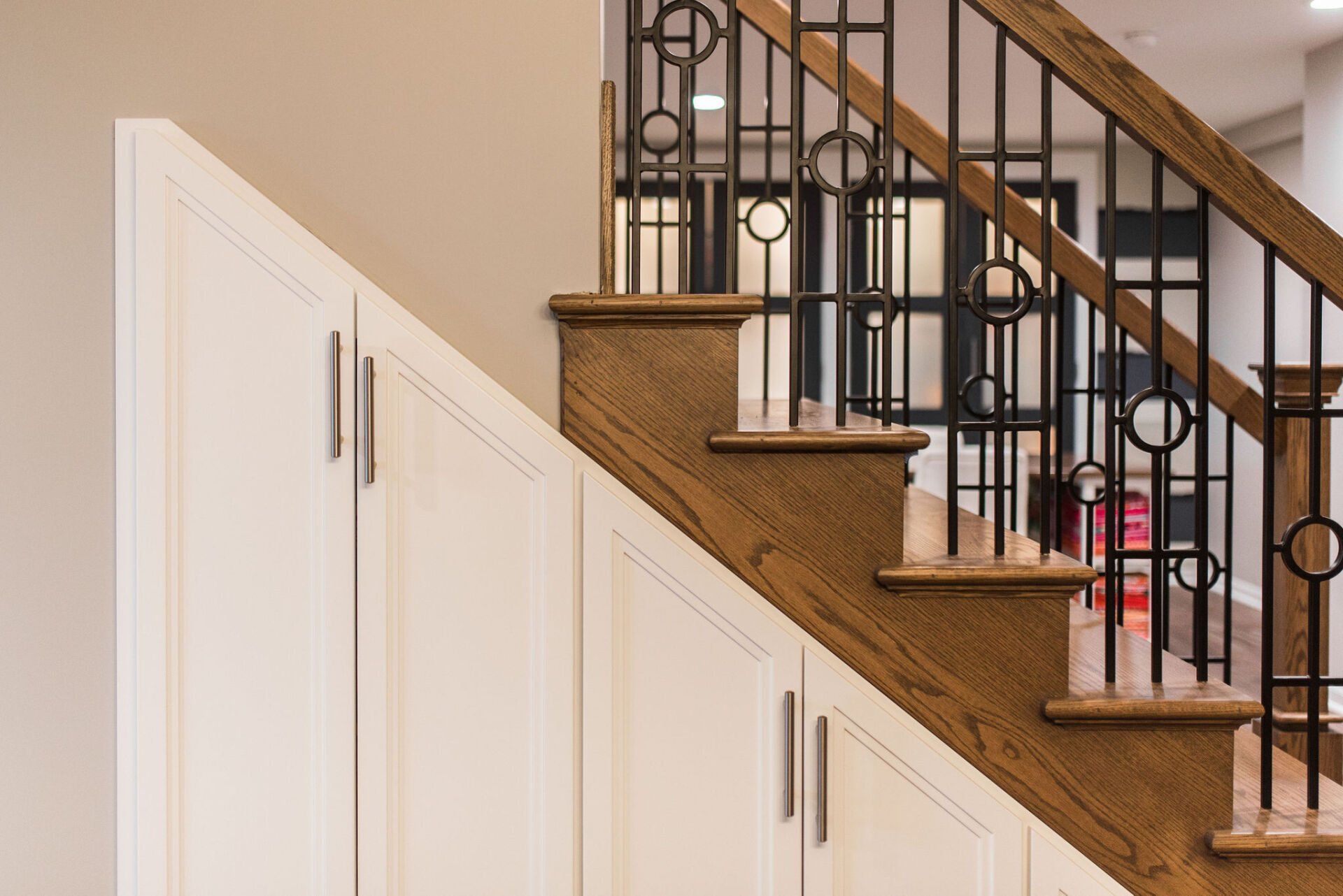 A wooden staircase with a metal railing and white cabinets underneath it.