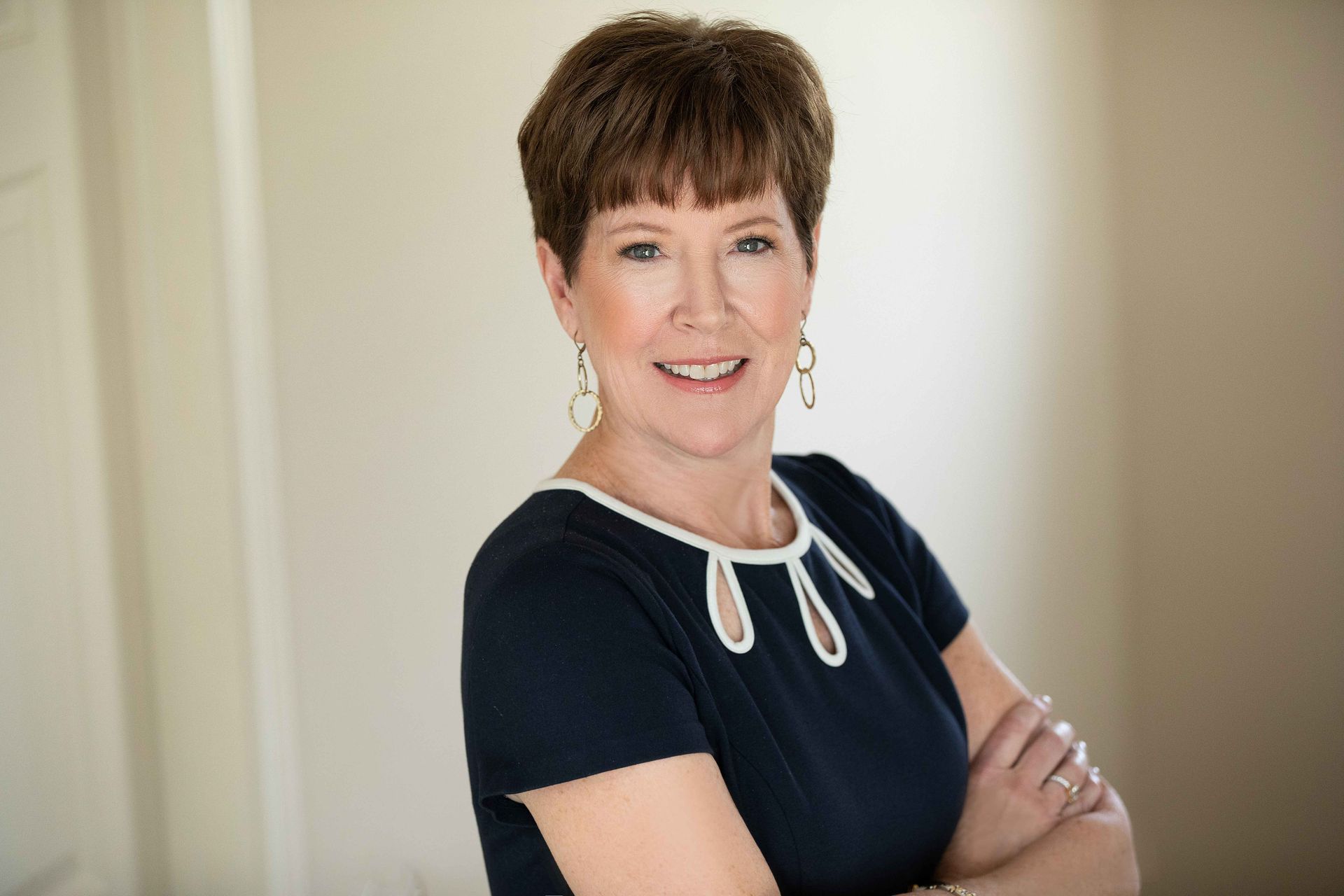 A woman in a blue dress is standing with her arms crossed and smiling.