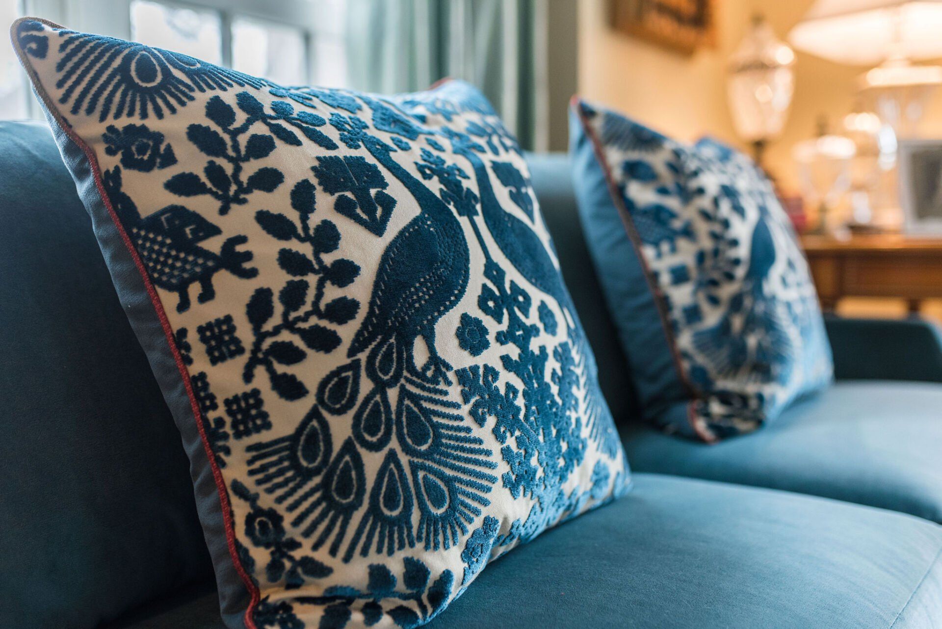 A blue couch with a peacock pillow on it.