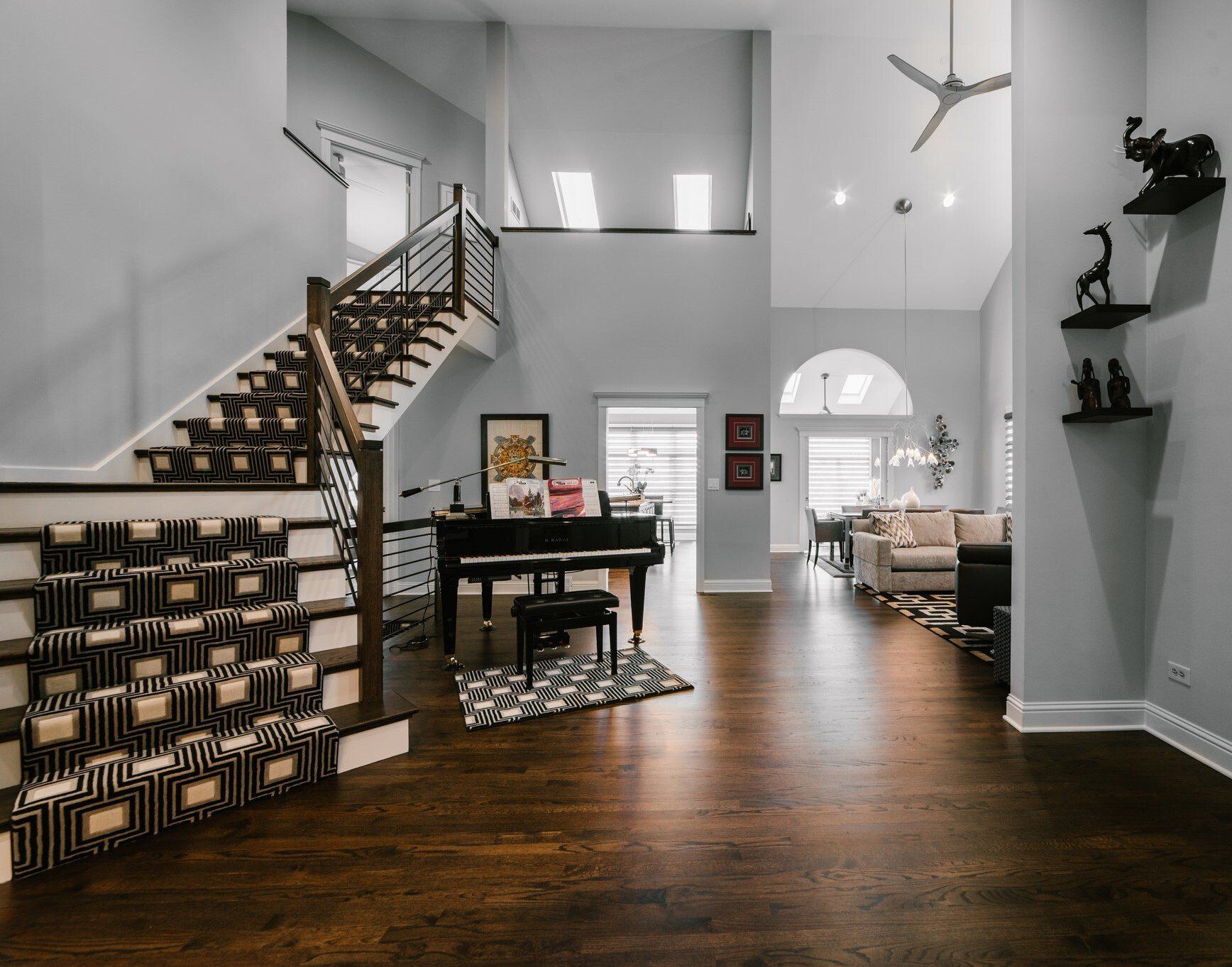 A living room with a piano and stairs in a house.