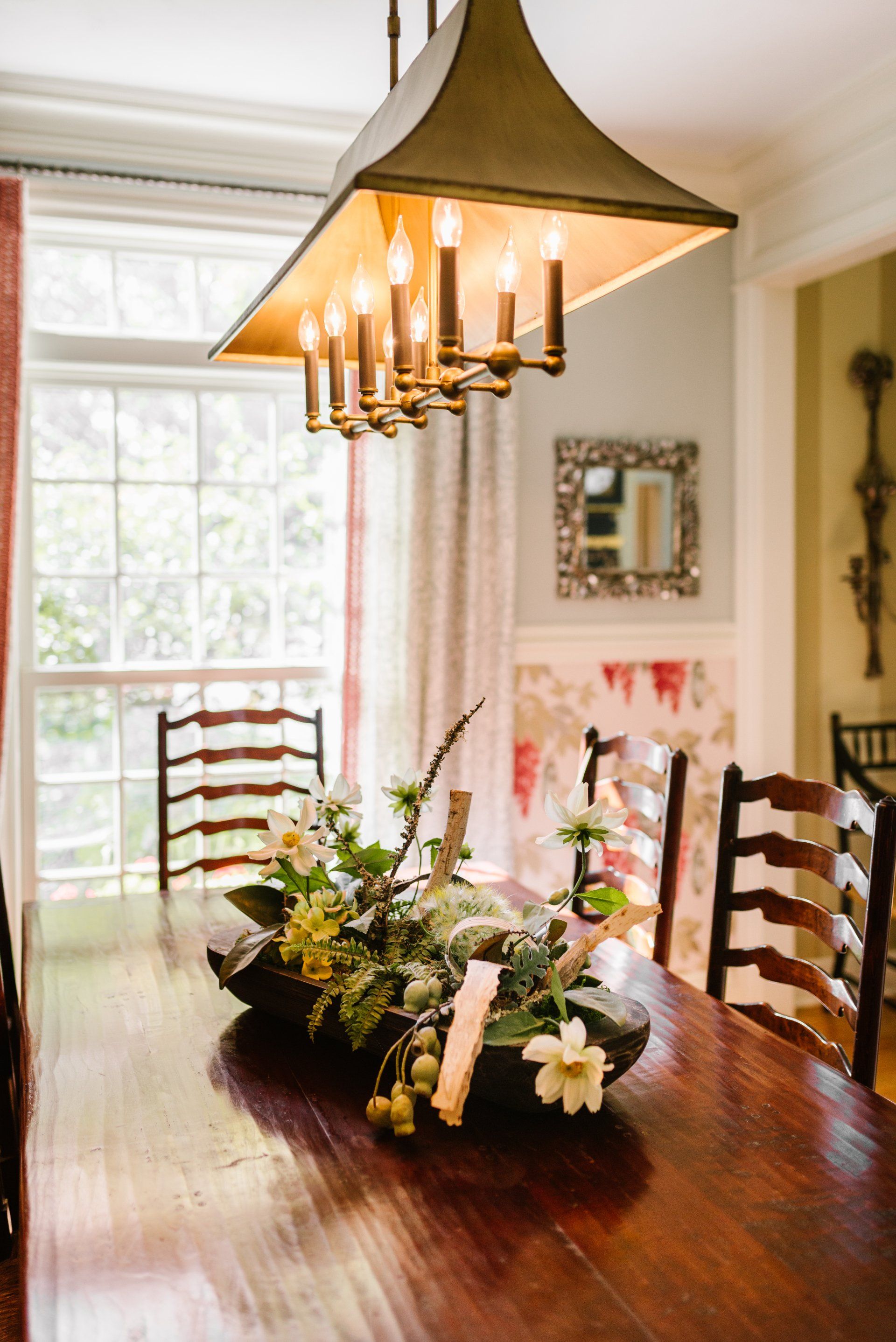 A dining room table with a bowl of flowers on it and a chandelier hanging from the ceiling.