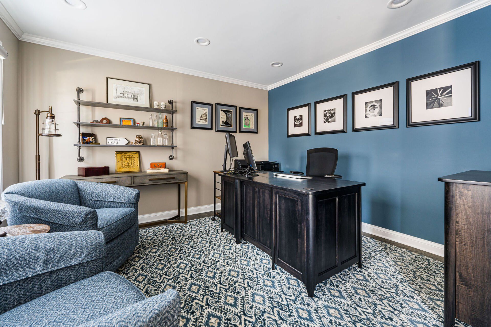 A home office with a desk , chairs , shelves and pictures on the wall.
