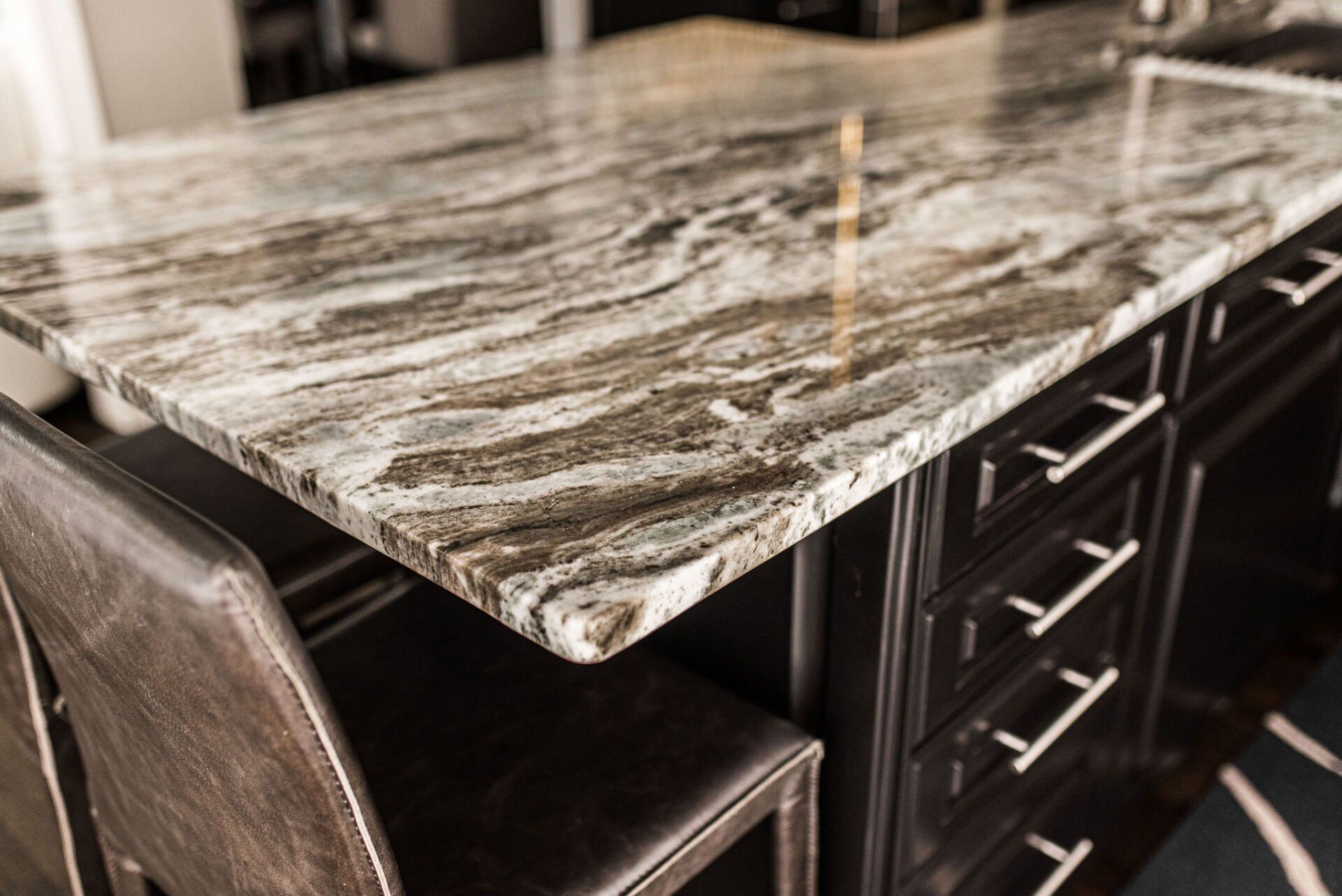 A kitchen island with a granite counter top and two chairs.