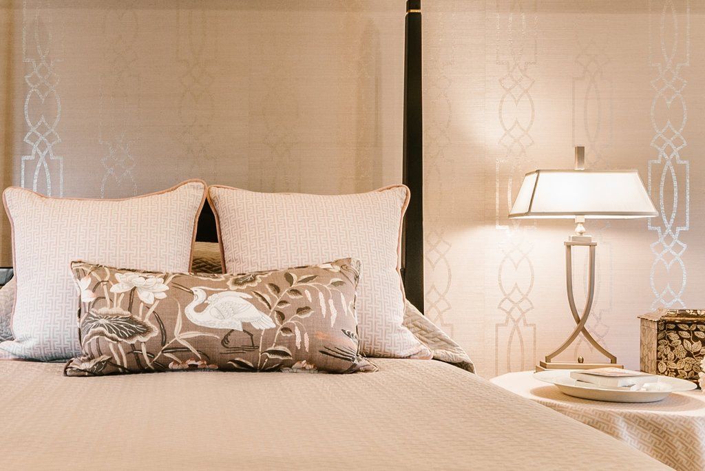 A bedroom with a four poster bed , pillows , a lamp and a table.