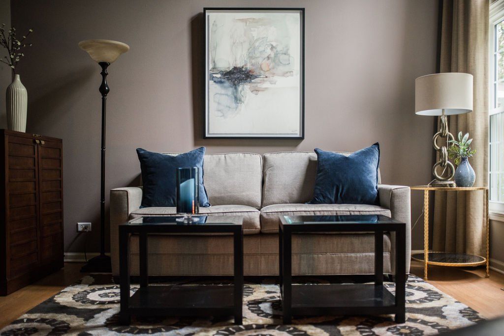 A living room with a couch , two coffee tables , and a painting on the wall.