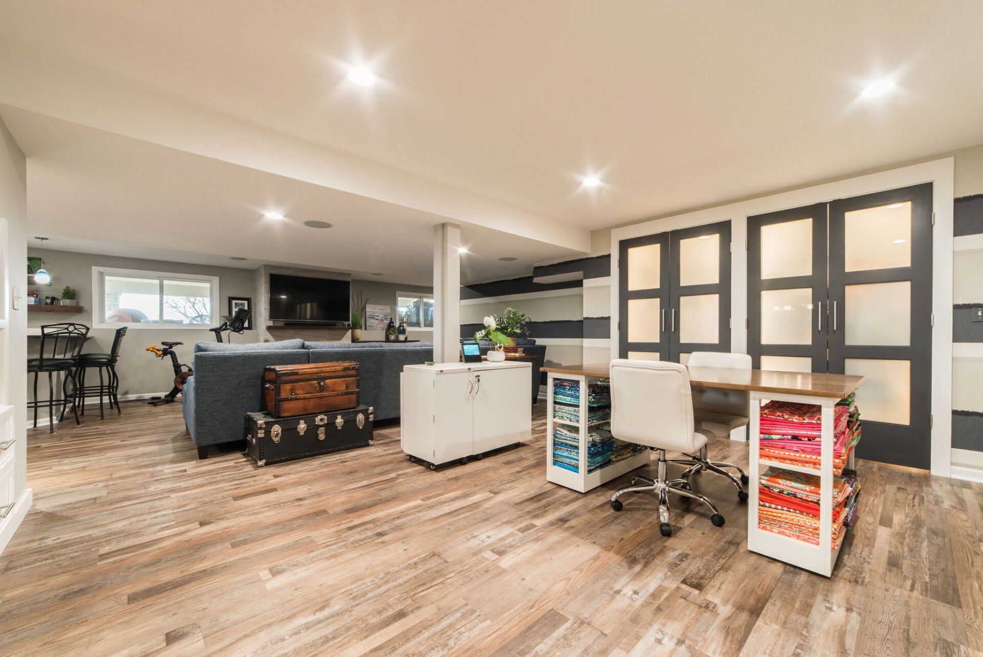 A basement with hardwood floors , a desk , chairs and a trunk.