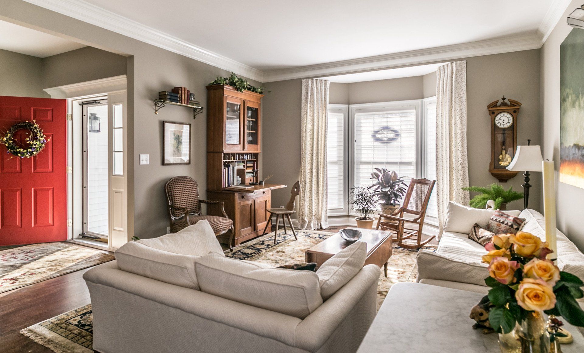 A living room with a couch , chairs , a clock and a red door.