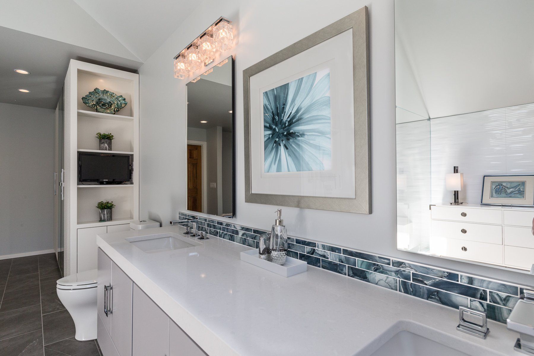 A bathroom with a sink , toilet , mirror and picture on the wall.