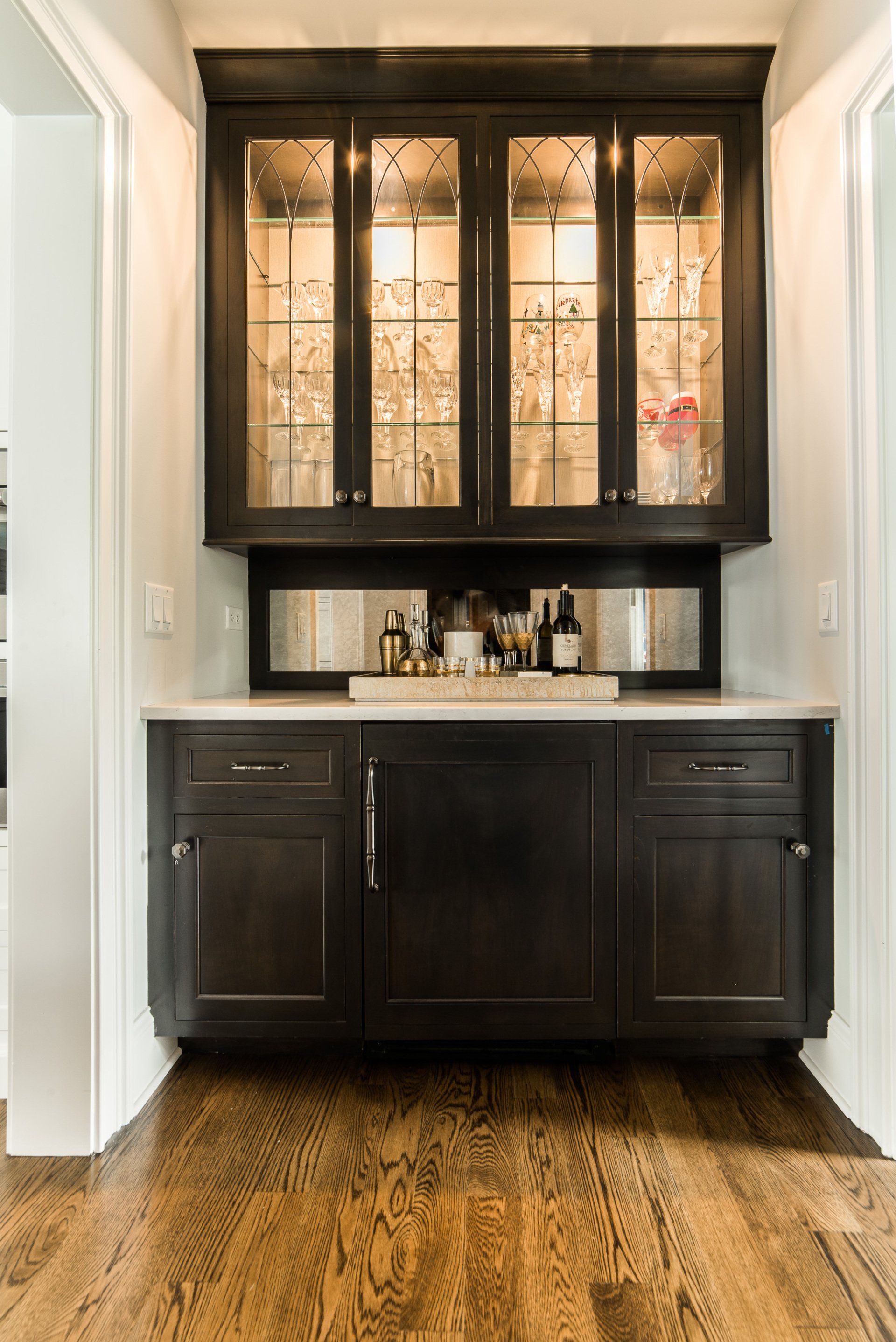 A kitchen with black cabinets and a bar with glass doors.