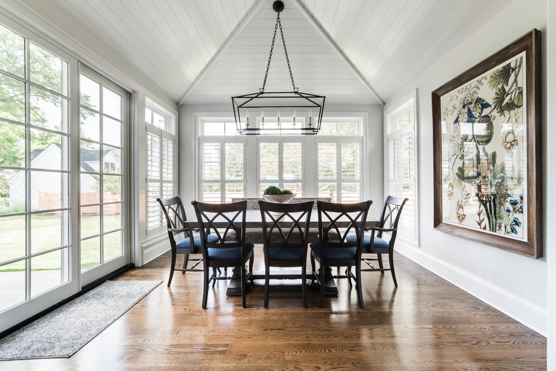 A dining room with a table and chairs and a painting on the wall.
