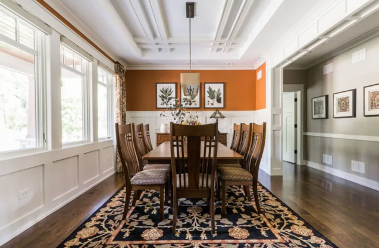 A dining room with a long table and chairs and a rug.