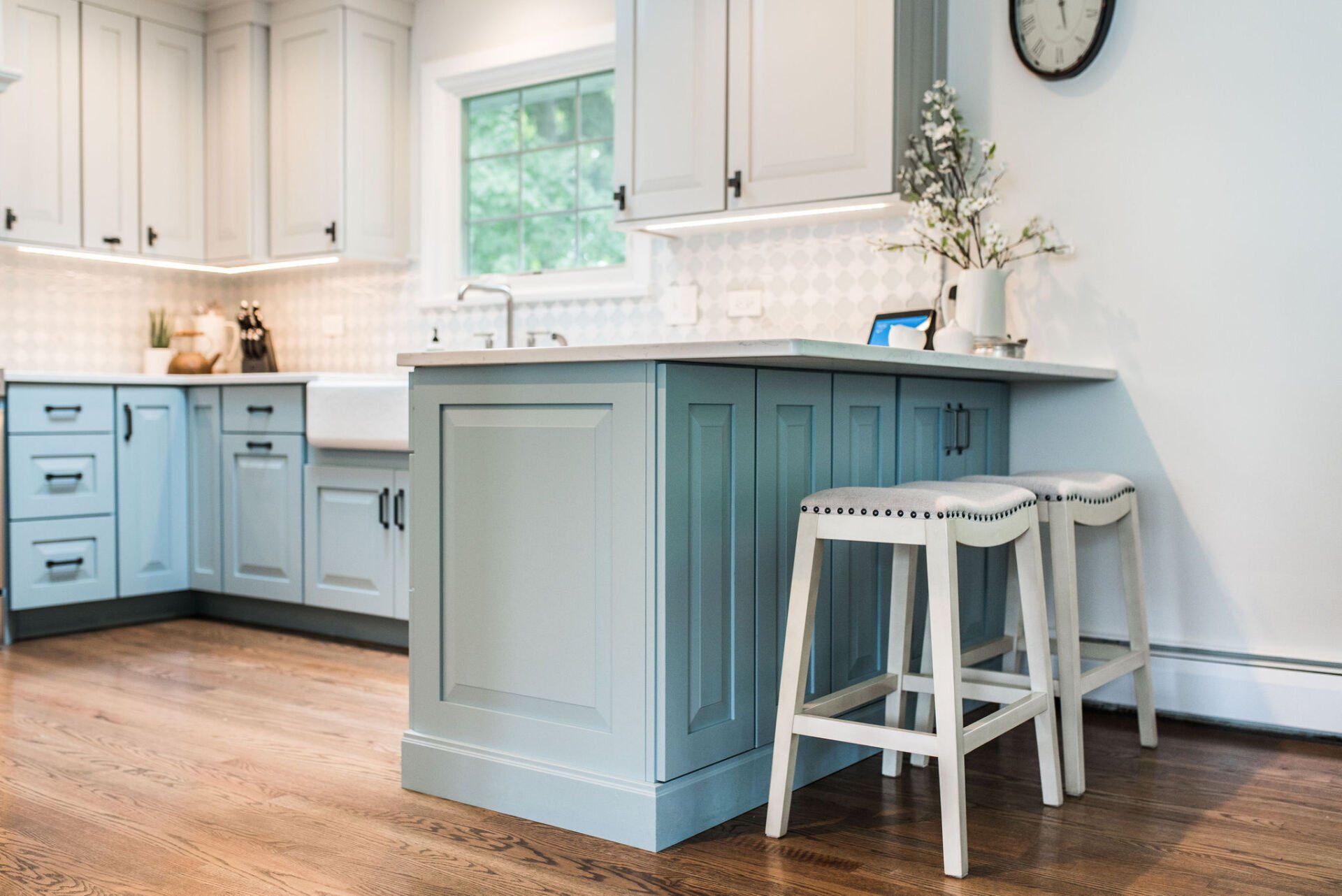 A kitchen with blue cabinets and white stools and a clock on the wall.