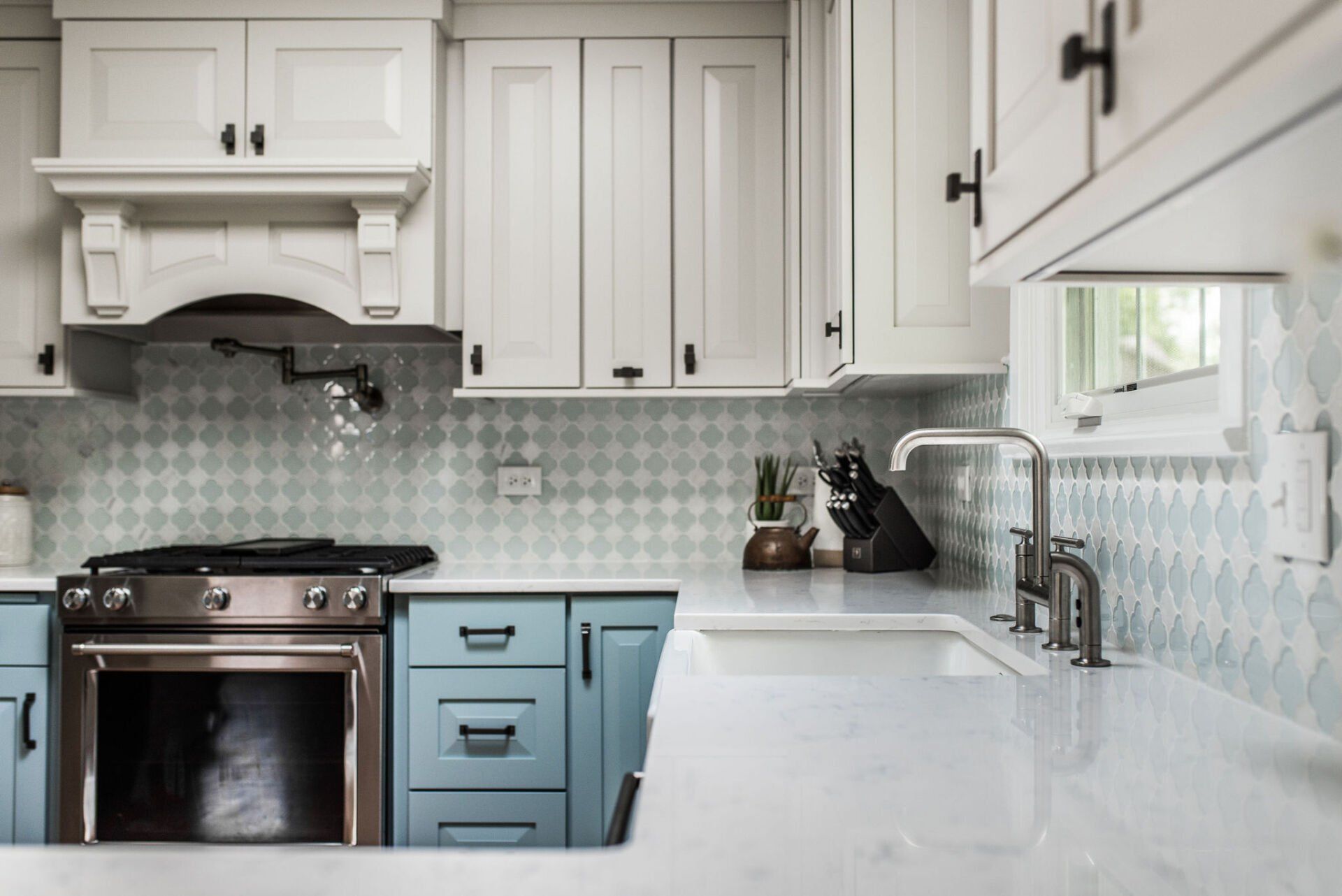 A kitchen with blue cabinets , white cabinets , a stove , a sink , and a window.