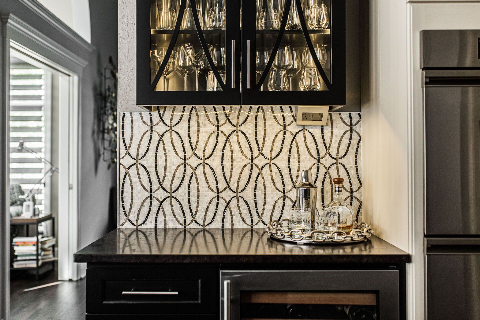 A kitchen with black cabinets , a wine cooler , a refrigerator and a bar.