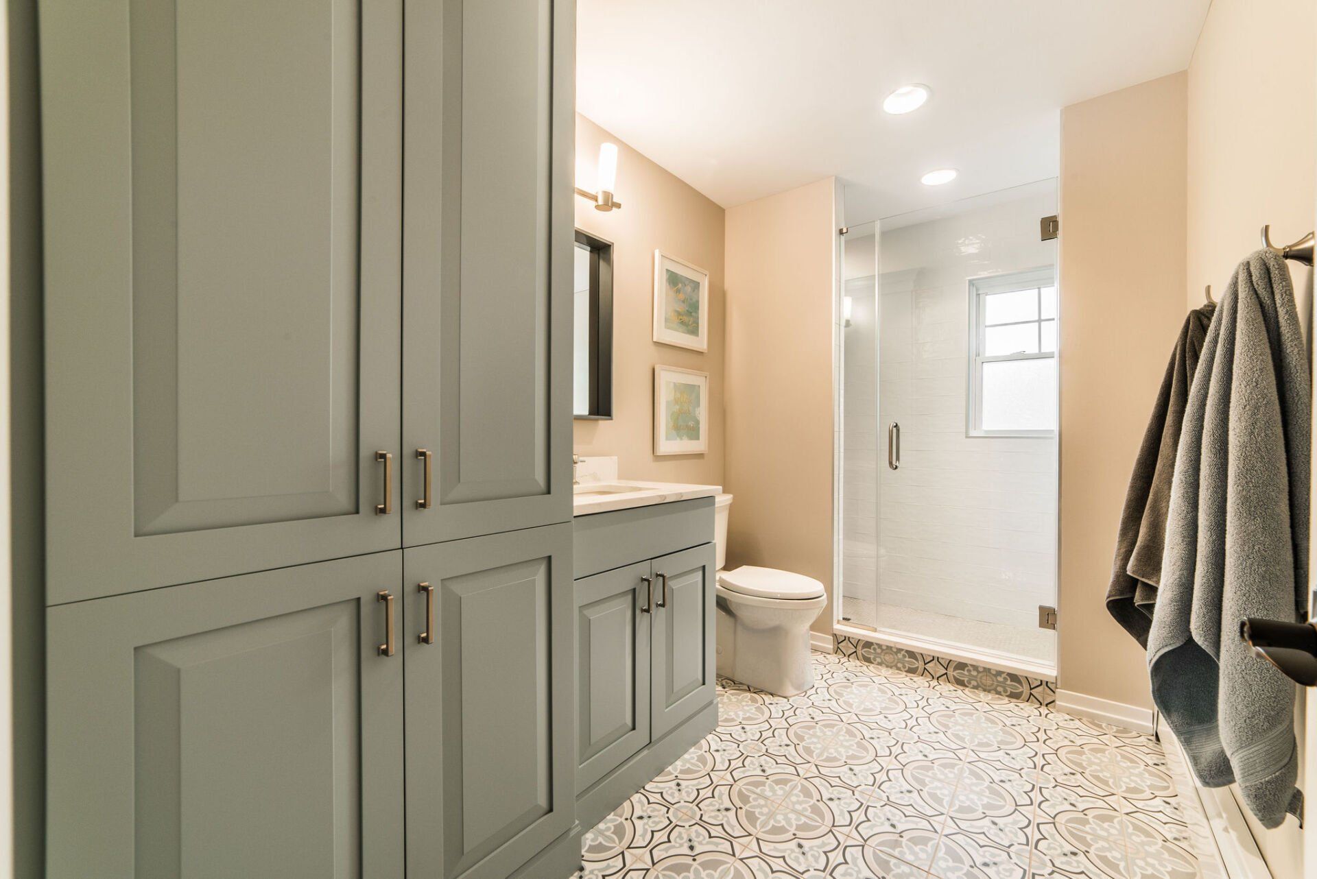 A bathroom with a toilet , sink , cabinets and a walk in shower.