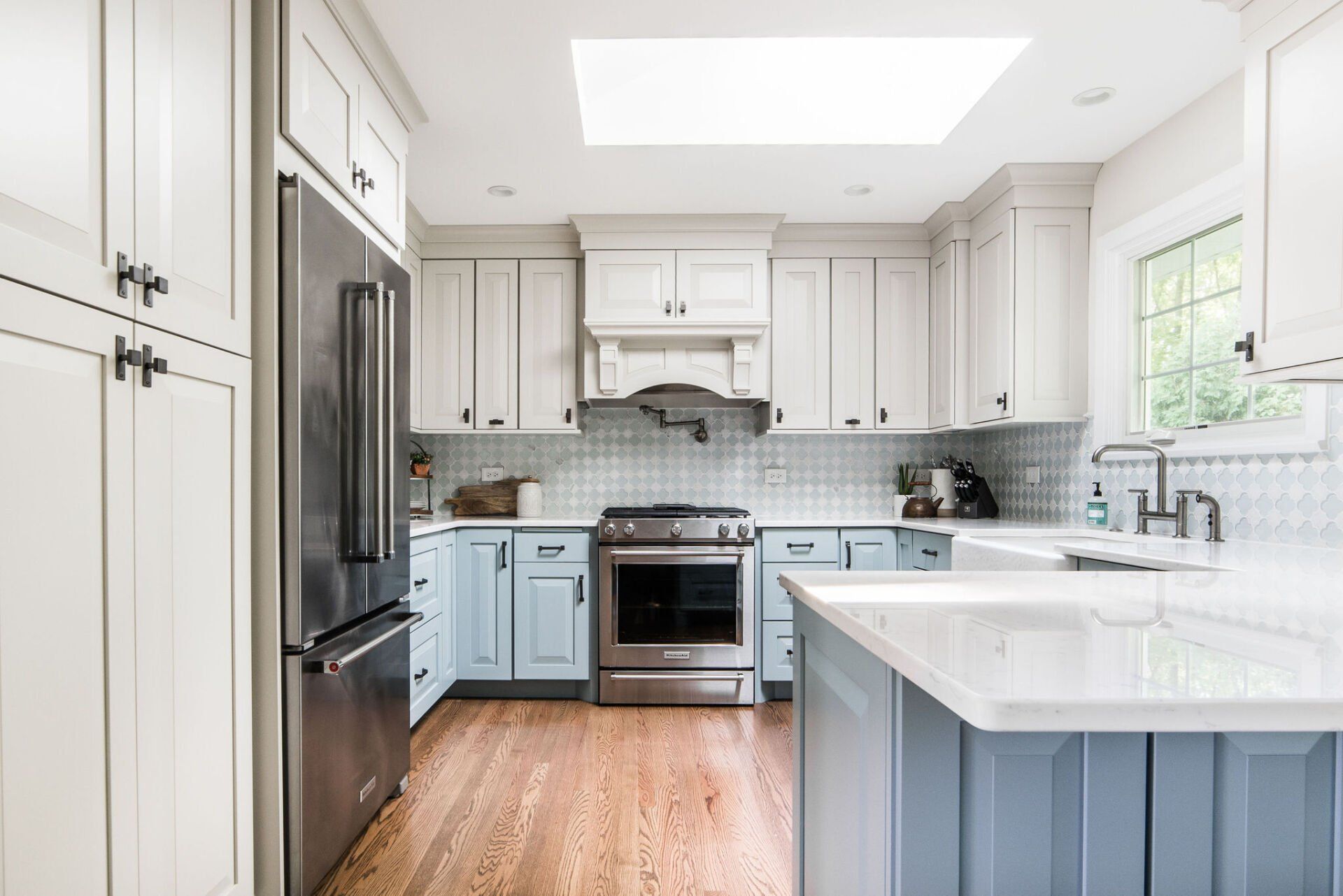 A kitchen with white cabinets , blue cabinets , stainless steel appliances and a skylight.