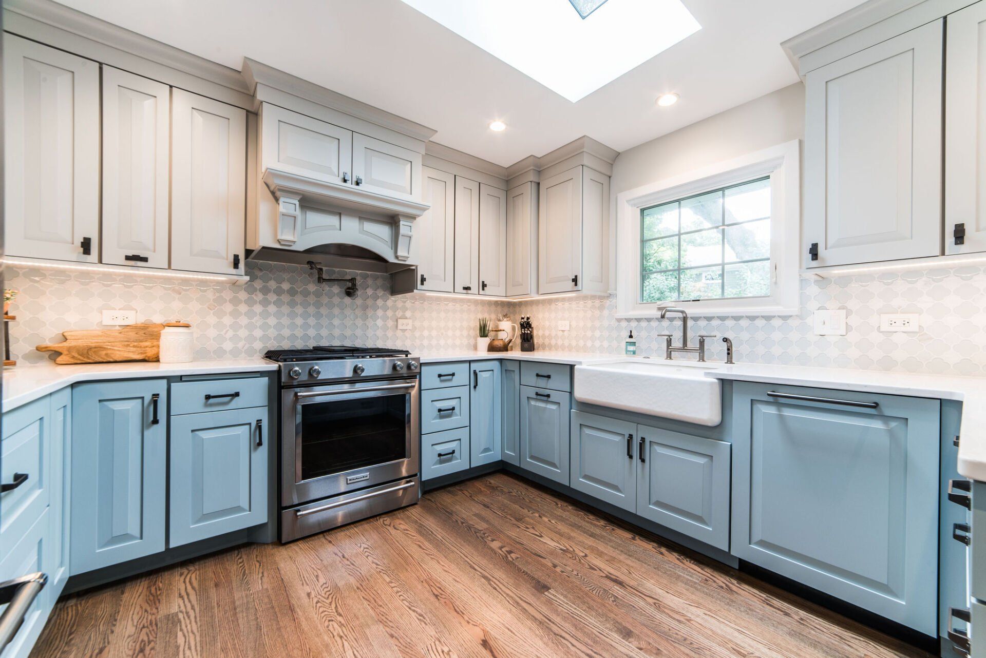 A kitchen with blue cabinets , a stove , a sink , and a skylight.