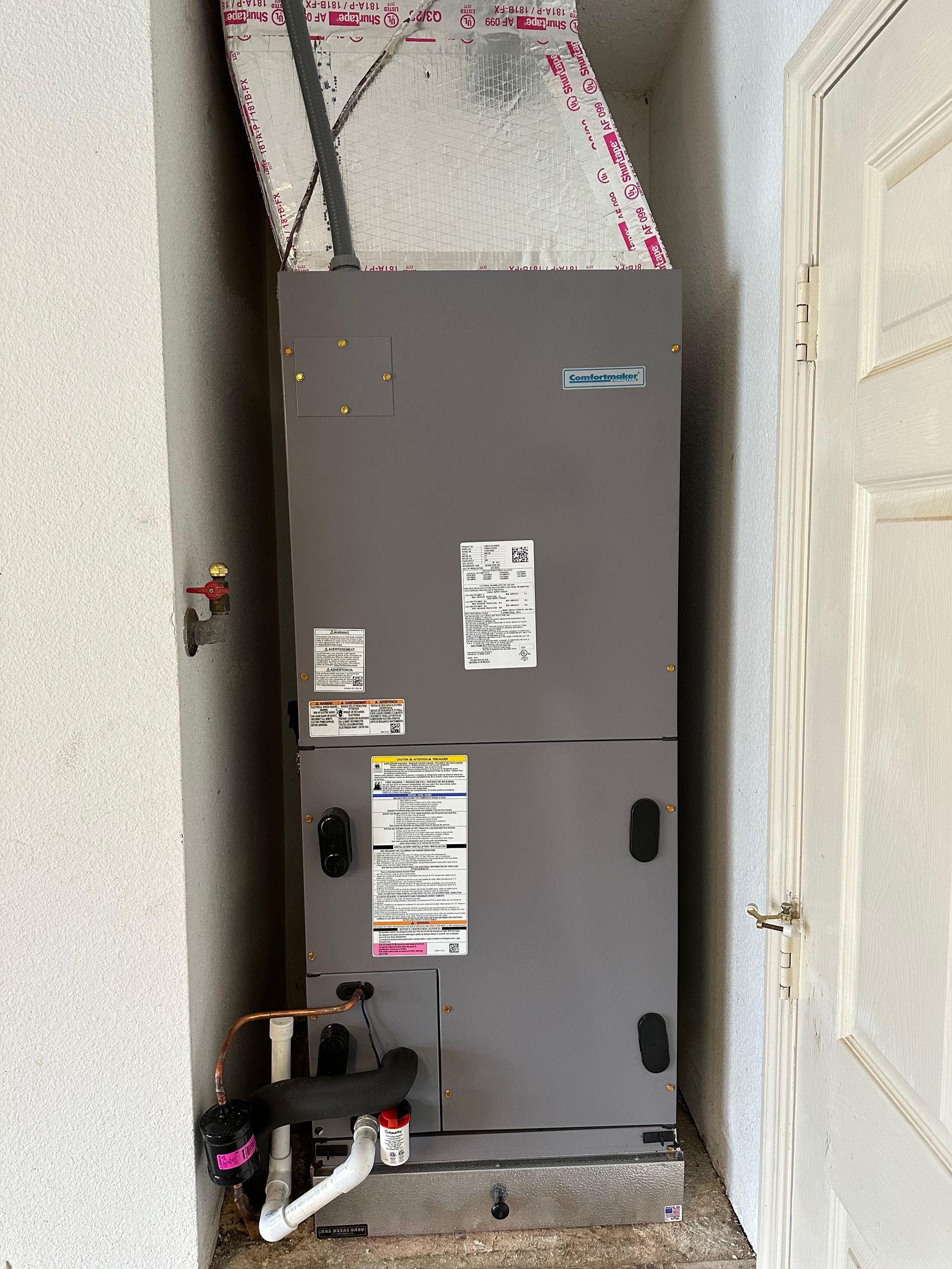 a gray air conditioner is sitting in a corner of a room next to a door .