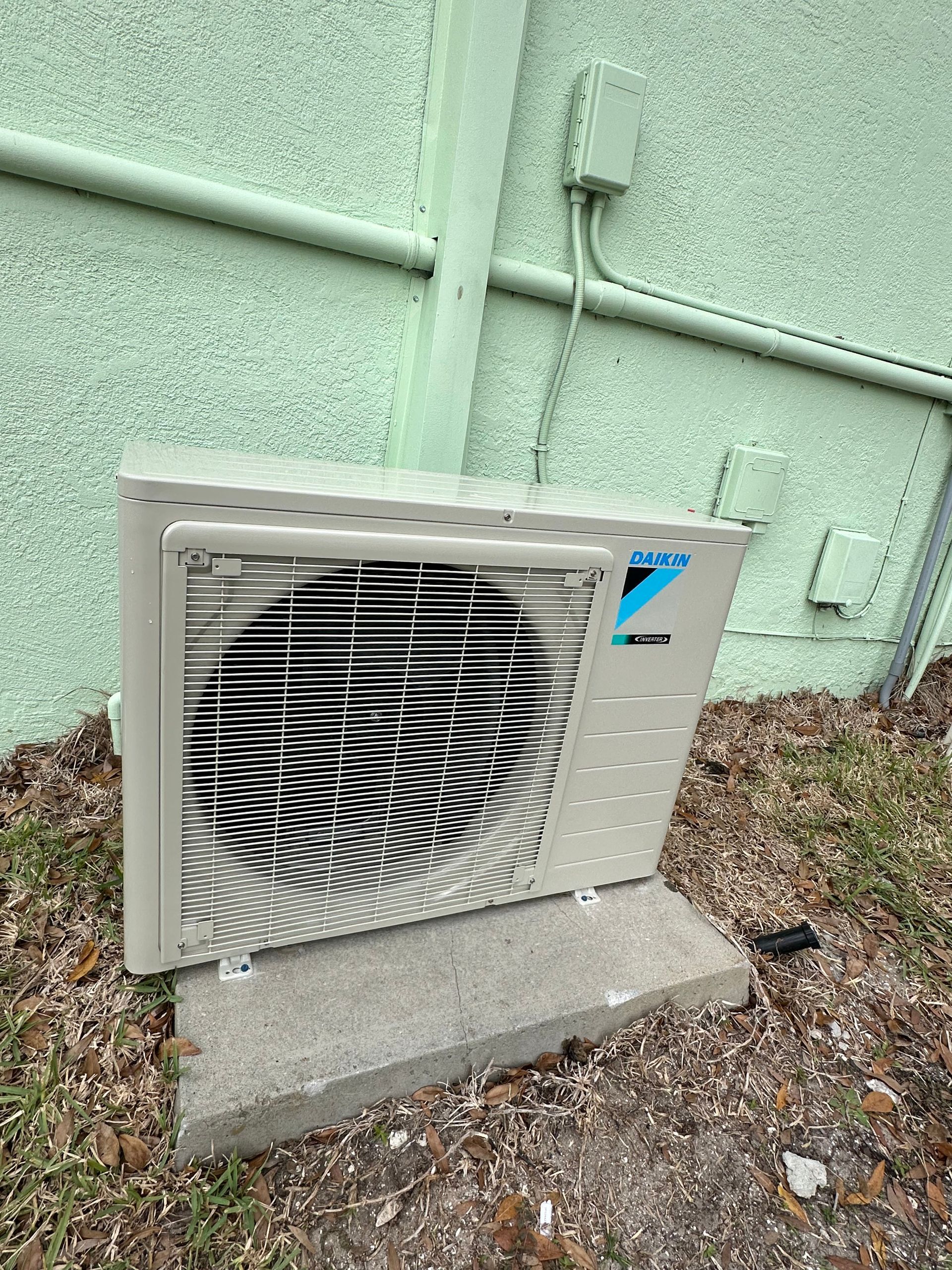 a white air conditioner is sitting on top of a concrete block next to a green wall .