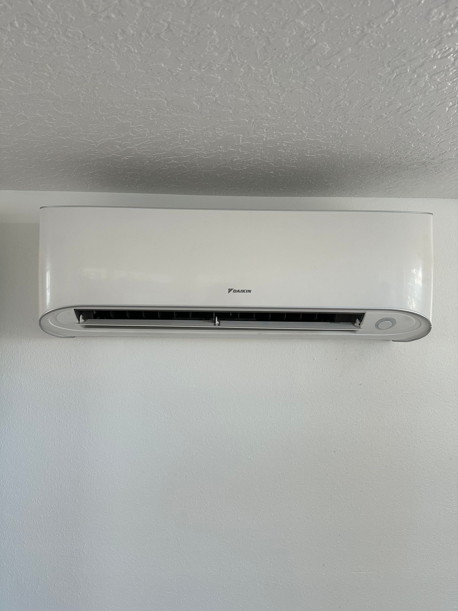 a white air conditioner is hanging on a white wall .